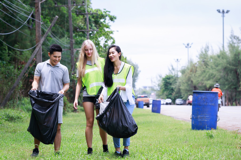 CSR activity. Corporate Social Responsibility. Three volunteers, Asian male, female and Caucasian are helping to pick up waste by garbage bags beside the road. Environmental problem. Environment day