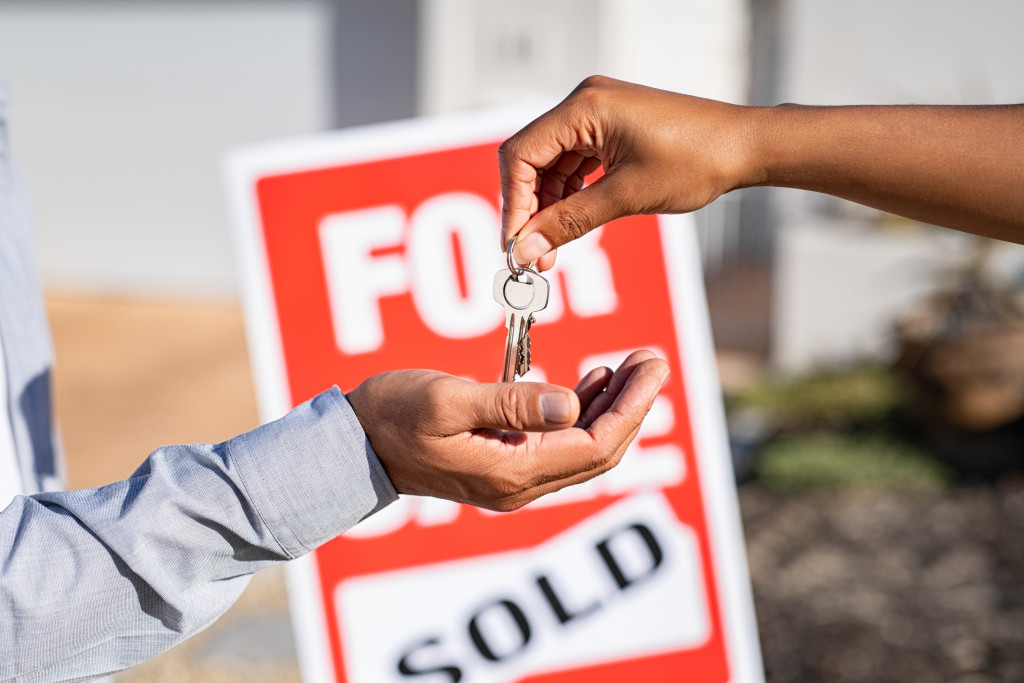 saleswoman giving home keys to new buyer against sold sign